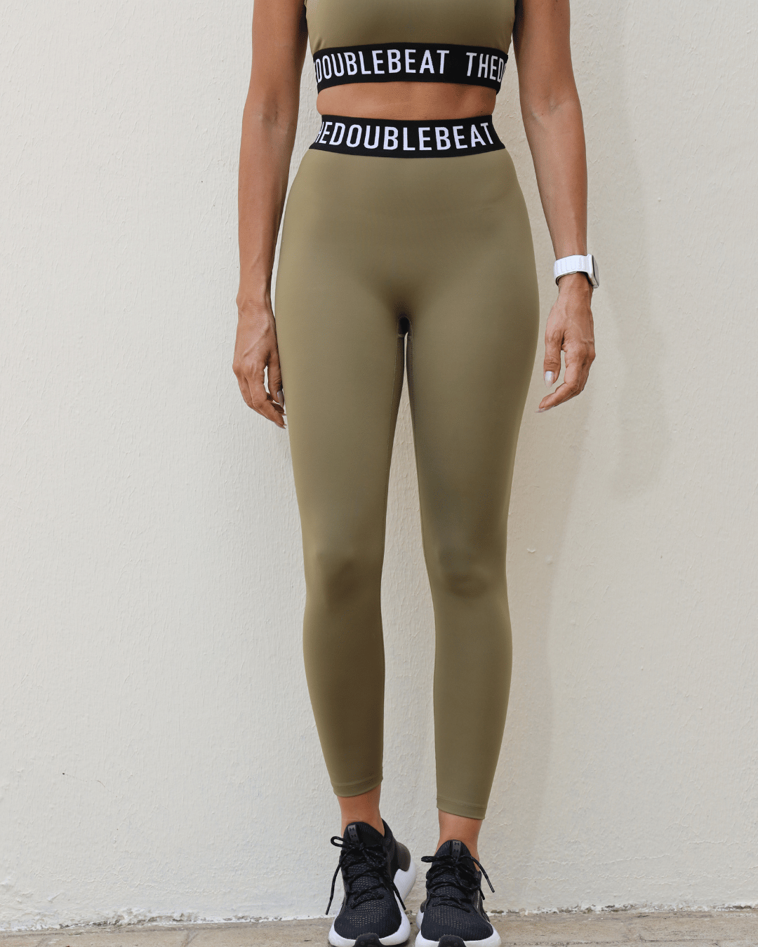 Women wearing olive green leggings with a matching top on a white background