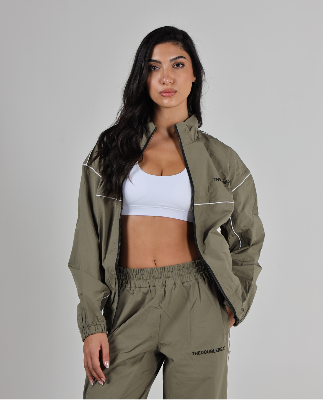 Woman wearing an olive green tracksuit with a white top on a gray background