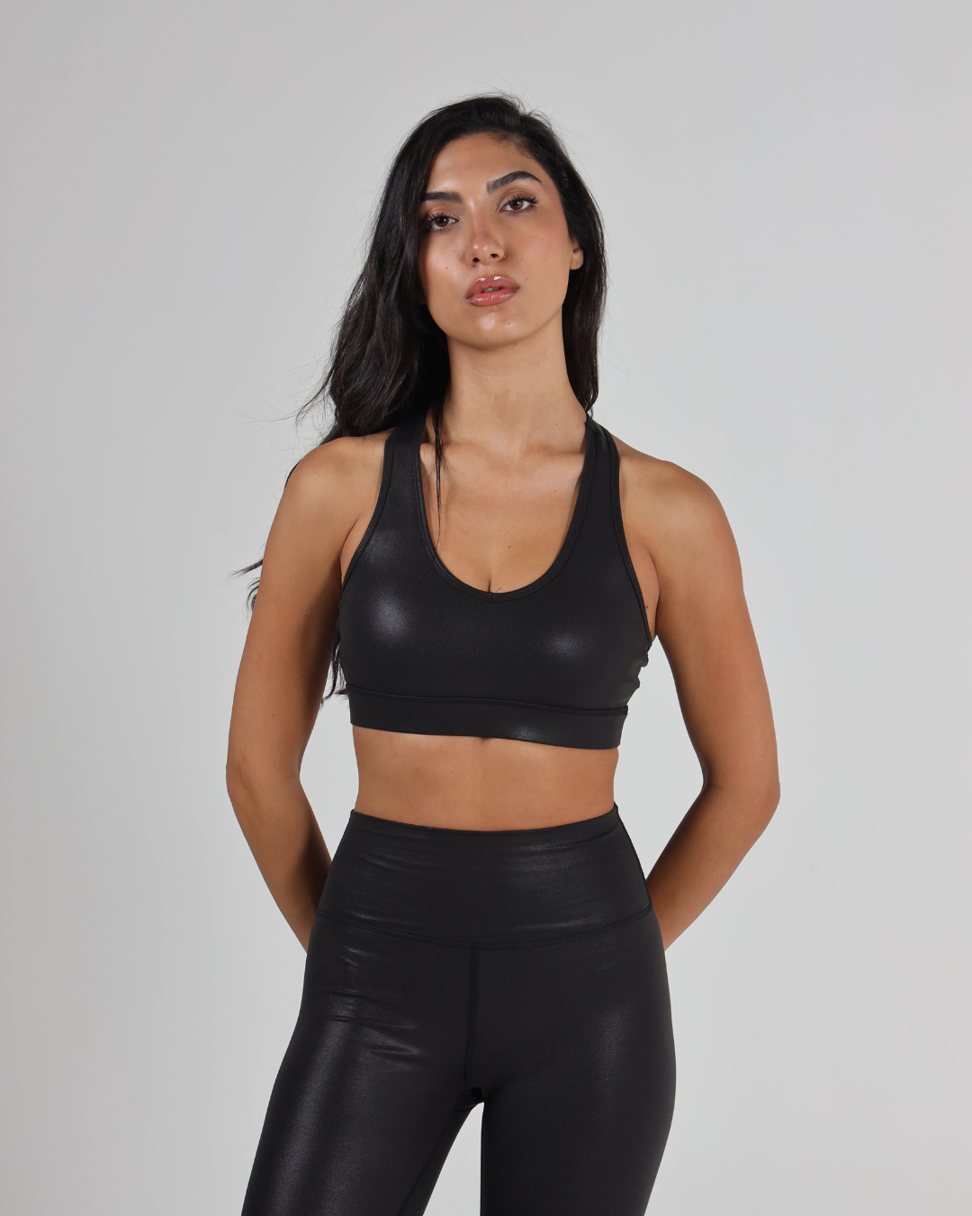 Woman wearing a black sports bra and leggings against a gray background