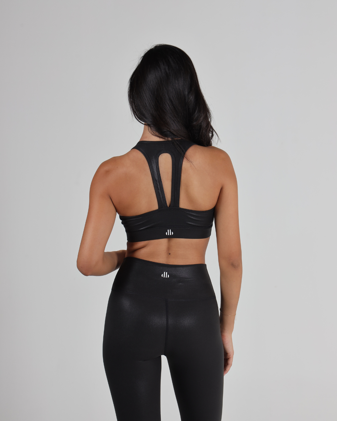 women wearing a black sports bra and leggings with a brand logo on a gray background