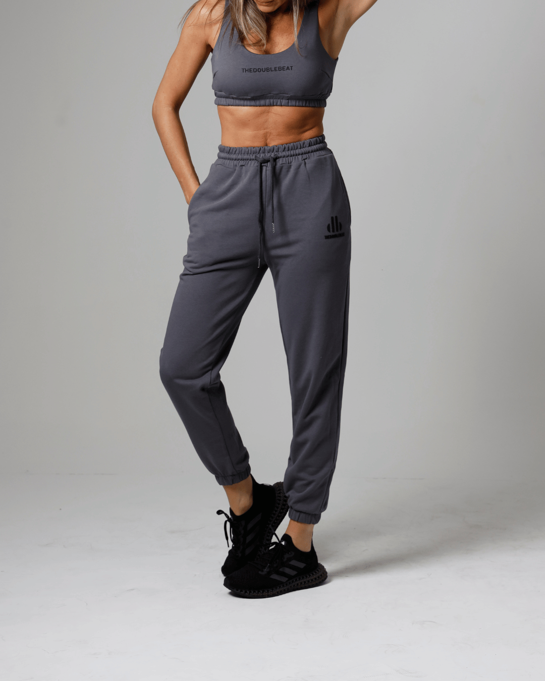 women wearing a gray athletic outfit with a logo on a plain background