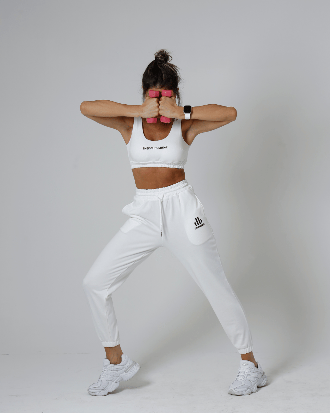 women in white athletic wear with Adidas logo lifting pink dumbbells against a gray background