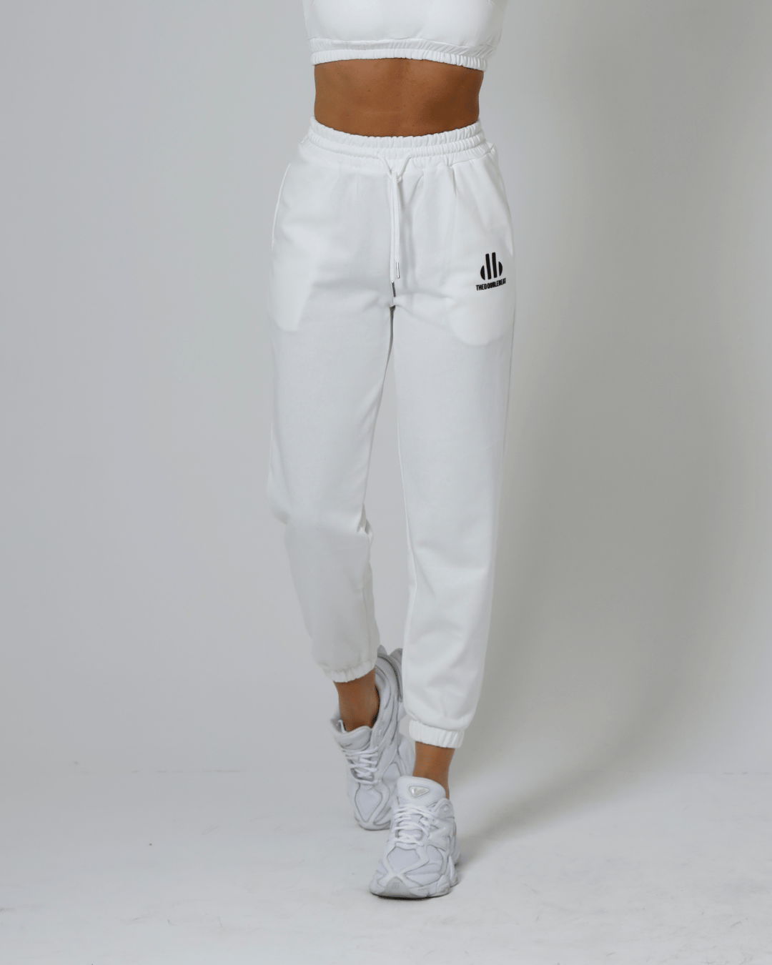 women wearing white jogger pants with a brand logo on a plain background