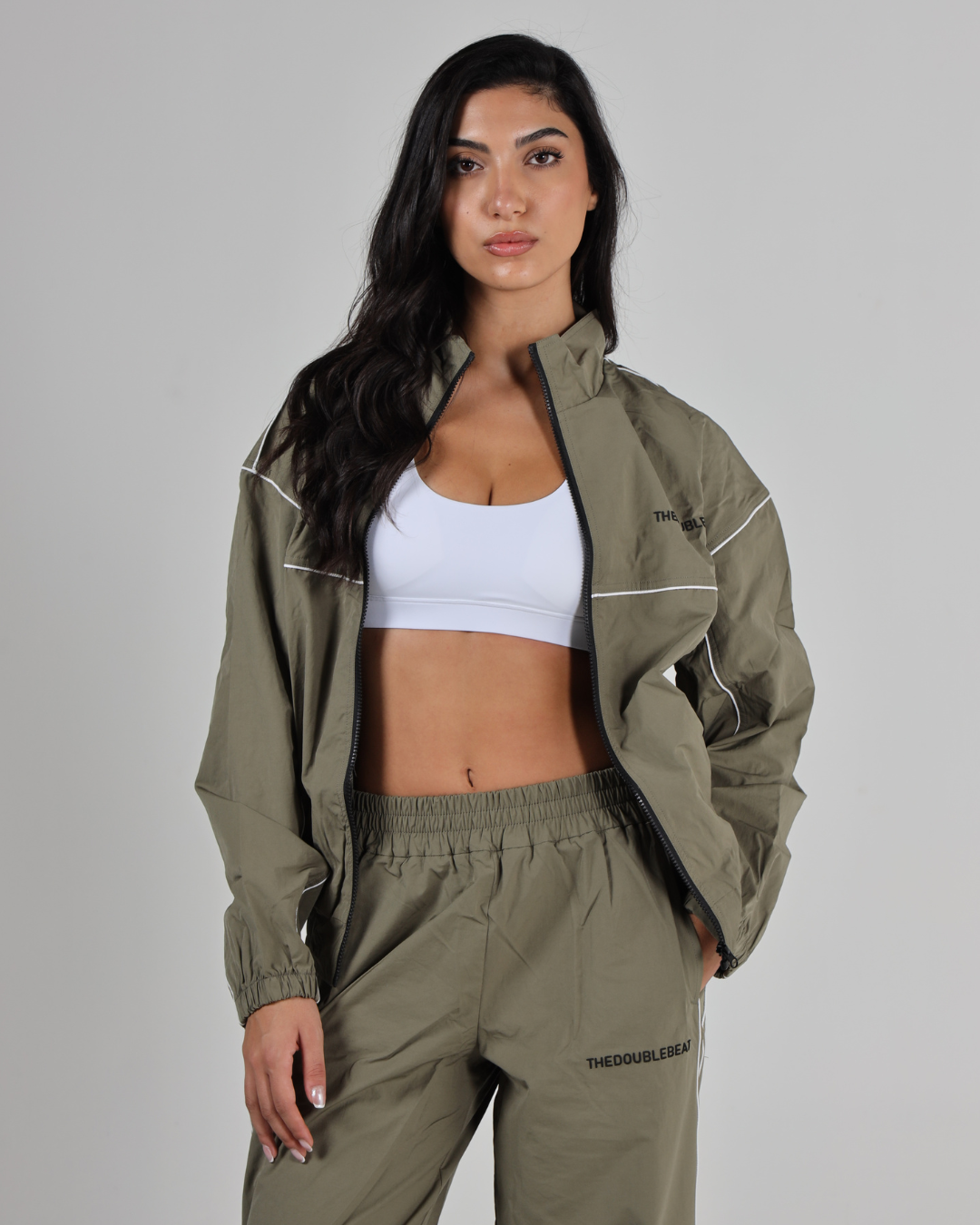 Woman wearing a green tracksuit with a white top against a gray background