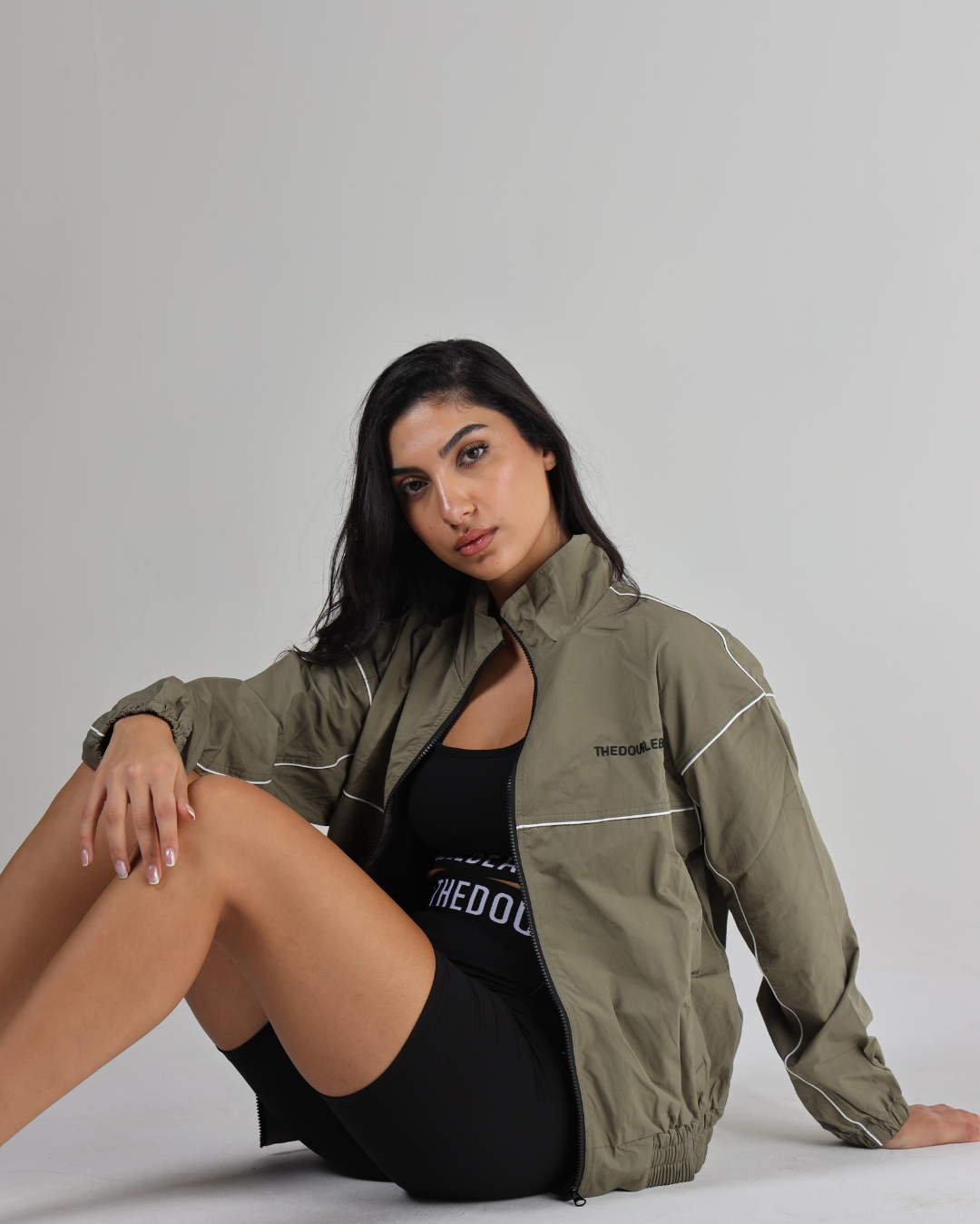 Woman wearing a green jacket sitting on the floor against a gray background