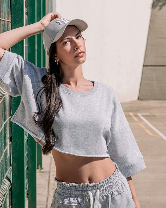 Woman wearing a gray crop top and cap leaning against a green wall.