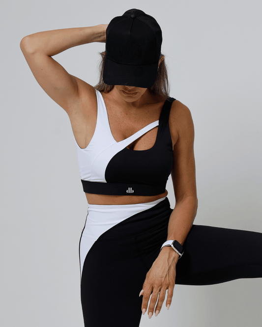 Women wearing a black and white sports outfit with a cap on a plain background