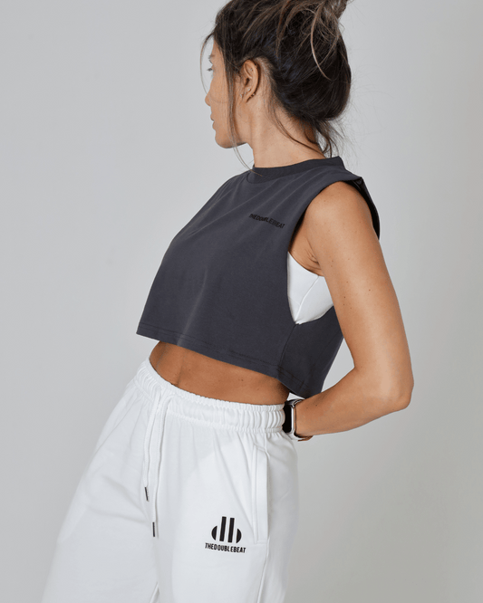 Person wearing a black sleeveless top and white pants with a logo on a gray background